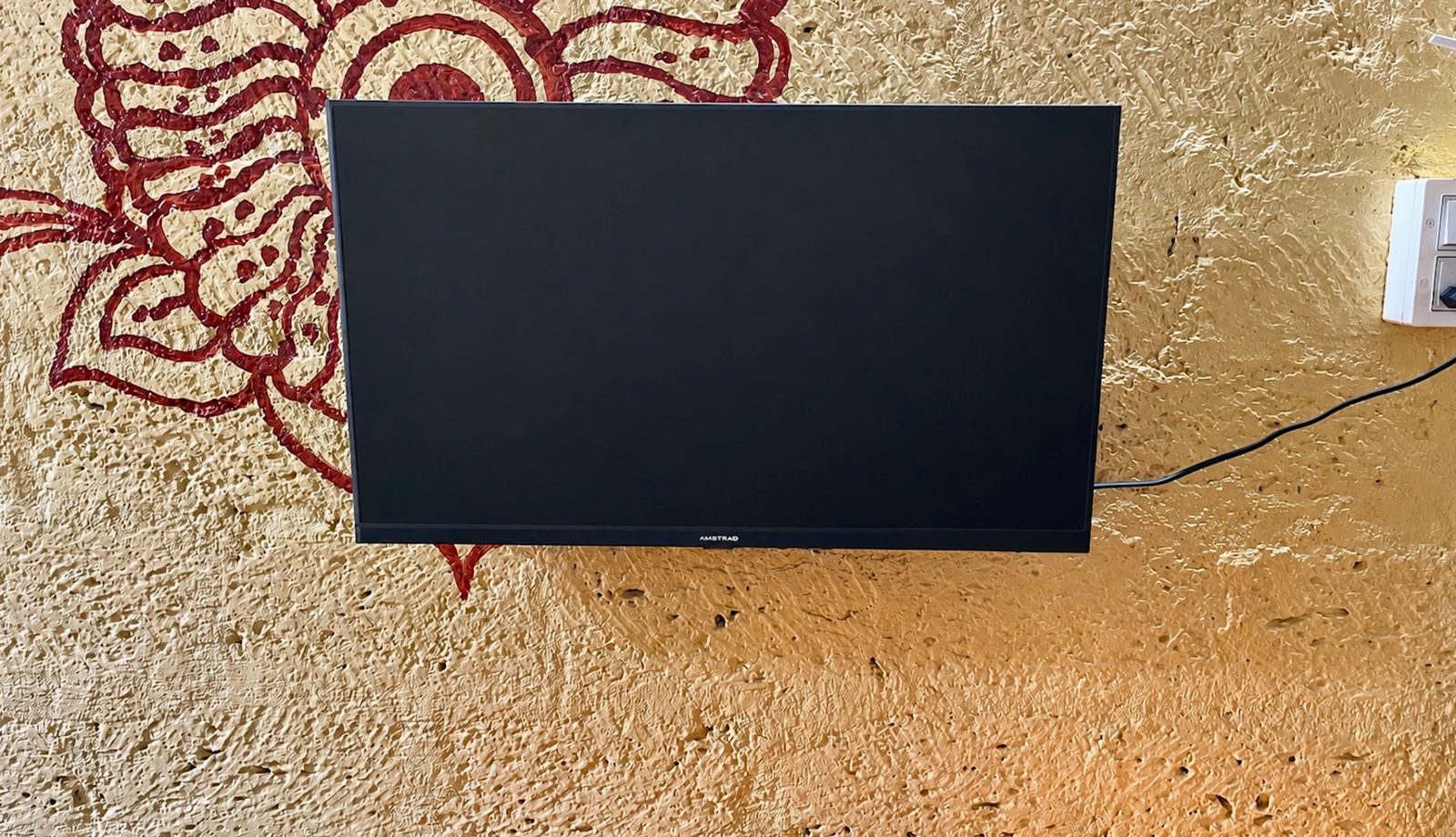A wall-mounted television on a hand-painted ochre wall in a resident common area